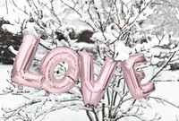 Pink gold love balloon word hanging on a snowy tree