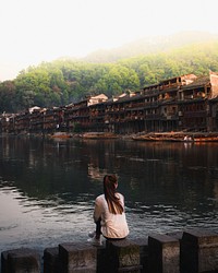 Woman sitting by a river at Fenghuang Ancient Town​​​​​, China