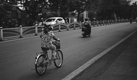 Vietnamese woman riding a bike on a road in grayscale
