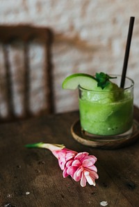 Green apple smoothie with a red ginger flower on a wooden table