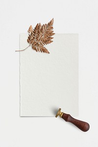 Dried brown leaf on white paper with a wax seal stamp flatlay