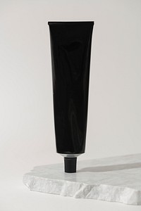 Black aluminium collapsible tube, beauty product packaging, on marble product stand