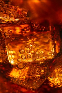 Cold carbonated drink over ice cubes in a glass close up 