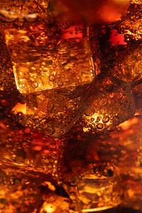 Cold carbonated drink over ice cubes in a glass close up 