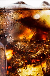 Cold carbonated drink over ice cubes in a glass close up 