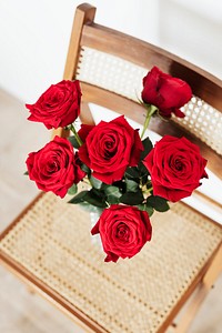 Red roses in a glass vase on a wooden chair