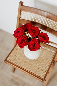 Red roses in a white vase on a wooden chair