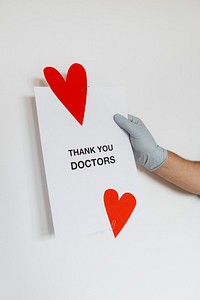 Gloved hand holding a thank you doctors card during the COVID-19 pandemic