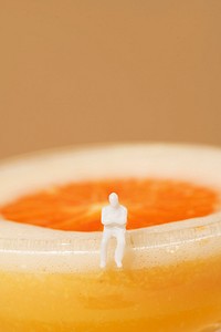 Tiny man sitting on the edge of an orange margarita cocktail