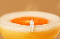 Tiny man sitting on the edge of an orange margarita cocktail