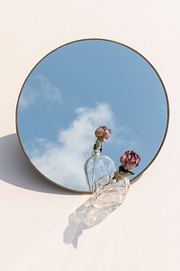 Dried pink rose in a glass bottle reflecting on a shiny tray