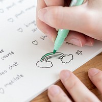 Girl coloring a rainbow doodle in a notebook