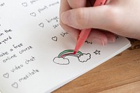 Girl coloring a rainbow doodle in a notebook