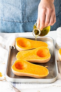 Woman drizzling olive oil over butternut squash before baking 