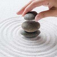 Hand stacking zen stones on the sand wellness background