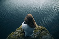 Man sitting on a cliff facing ocean view, free public domain CC0 photo.