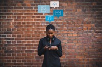 Black woman using her phone in front of a brick wall