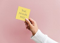 Woman holding a sticky note mockup against a pink wall