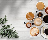 Mixed coffee cups with a leaf on a white wooden textured wallpaper