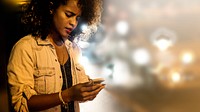 Black woman texting near the street at night