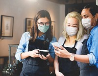 Happy baristas wearing masks looking at a phone in a cafe