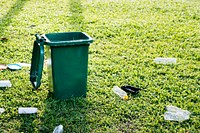 Recycling campaign with green bin and wasted plastic bottles on the field