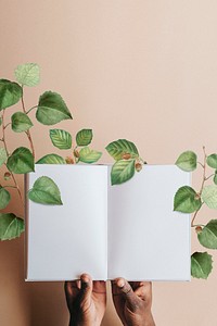 Hand holding blank notebook page with green leaves