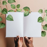 Hand holding blank notebook page with green leaves