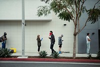 People using their phones and having social distancing while line up during coronavirus pandemic. Los Angeles, USA, April 4, 2020
