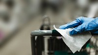 Gloved hand with a tissue paper on a shopping cart in a supermarket during the Coronavirus pandemic