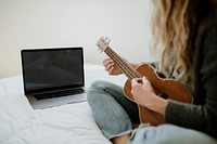 Woman using a laptop while playing ukulele during lockdown