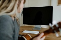 Woman using a computer while playing ukulele during quarantine 