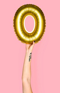 Tattooed hand holding golden letter O inflatable balloon