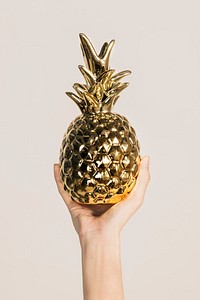 Hand showing a gold pineapple cup on a beige background