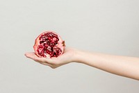 Hand holding a fresh cut pomegranate isolated on a gray background