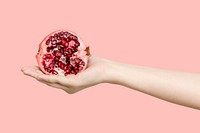 Hand holding a fresh cut pomegranate isolated on a pink background