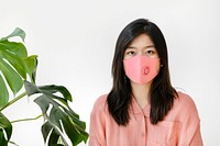 Asian woman wearing a mask standing next to a monstera plant