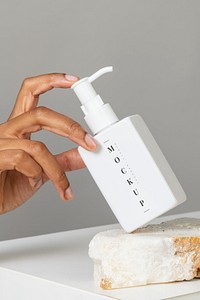 Hand arranging a blank white pump bottle on a stone mockup 