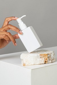 Hand arranging a blank white pump bottle on a stone