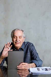 Senior man making video call from tablet computer with a mug and newspaper on the table