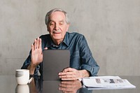 Senior man making video call from tablet computer with a mug and newspaper on the table 