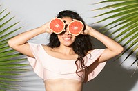 Cheerful woman covering her eyes with sliced grapefruit 
