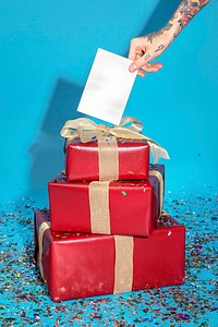 Tattooed hand holding a card with red gift boxes with confetti 