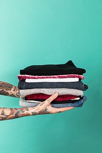 Tattooed hands holding a stack of folded clothes