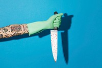 Tattooed feminine hand in a glove holding a knife