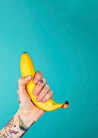 Tattooed hand with a ripe banana on blue background