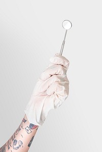 Tattooed hand in a white glove holding a dentist&#39;s mirror