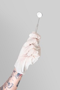 Tattooed hand in a white glove holding a dentist&#39;s mirror mockup