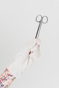 Tattooed hand in a white glove holding a surgical clip