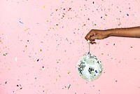 Woman holding a shiny silver disco ball in a confetti